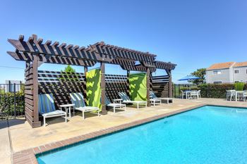 Swimming pool cabanas with lounge chairs, lime green curtain and blue patio umbrella in the distance1